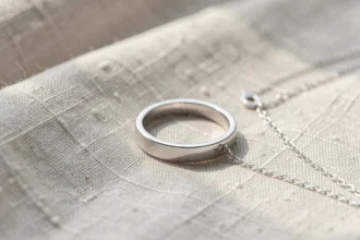 Bague et chaîne en or blanc posées sur un tissu clair