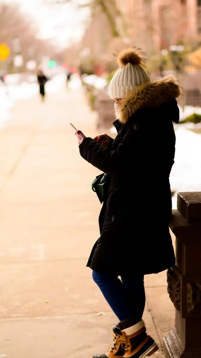 a woman standing on a sidewalk looking at her cell phone